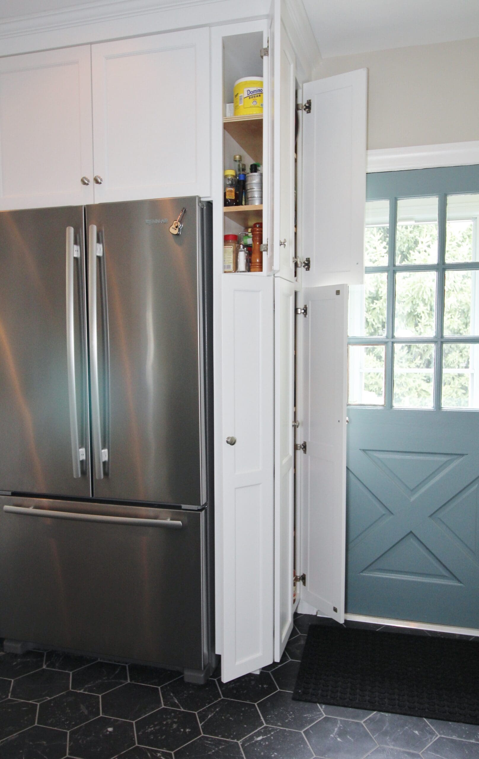 Small kitchen cabinetry. Cabinetry is finished in a white paint. Slim cabinets are opened to right of refrigerator showing how every inch of the space is functional.