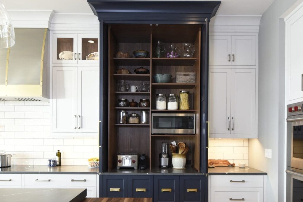Open navy kitchen appliance cabinet with wood interior shelves holding a microwave, toaster, dishes, and pantry jars in Edgewater, MD.