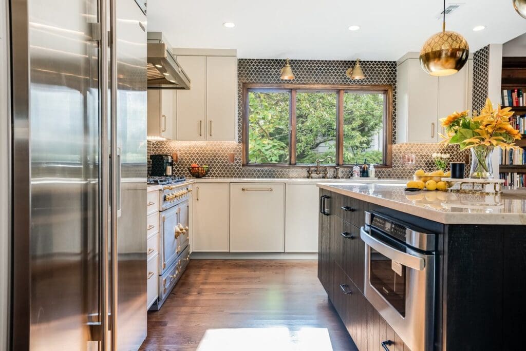 Light kitchen cabinets with gold-toned pulls paired with a dark wood island with dark hardware, metallic lighting, and stainless steel appliances.