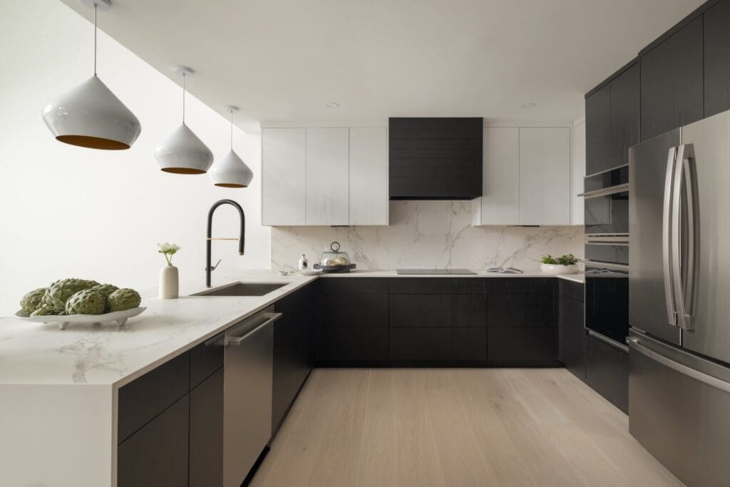 Modern kitchen with flat-panel black and white cabinets without visible pulls, white countertops, and stainless steel appliances in Ludlow, VT.