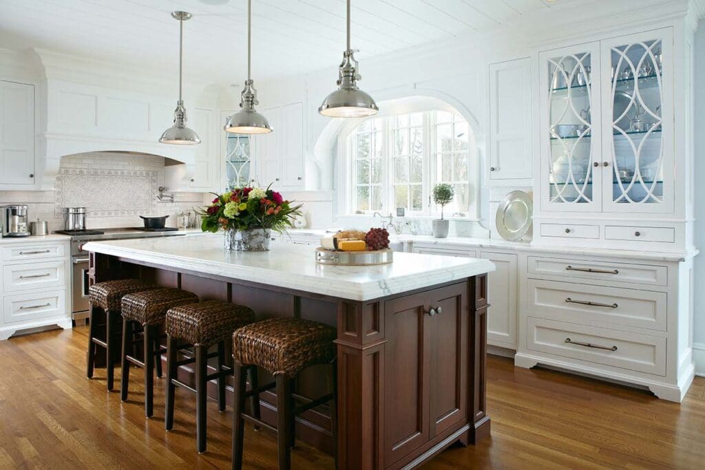 White glass-front kitchen cabinets with curved decorative mullions beside a dark wood island in New Canaan, CT.