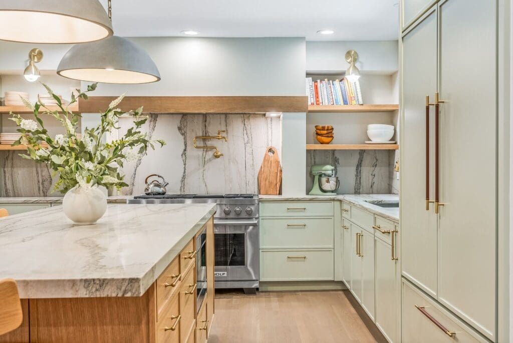 Green-gray slim Shaker kitchen cabinets with bronze pulls, wood shelves, and a wood-accented range hood.